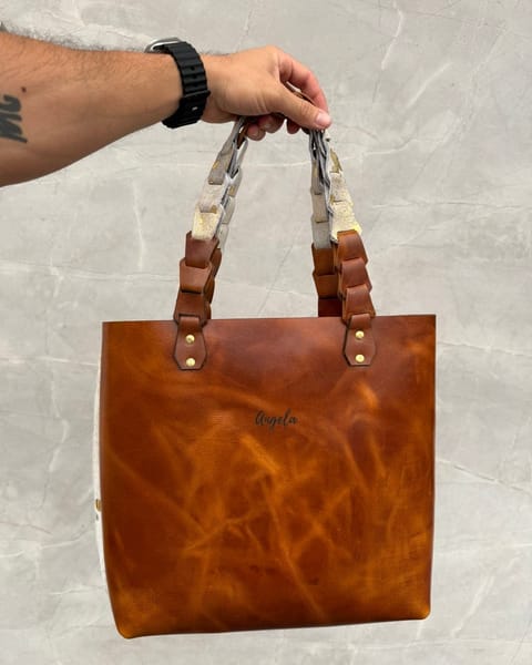 Bolso tote de cuero miel en la mano, con un nombre grabado