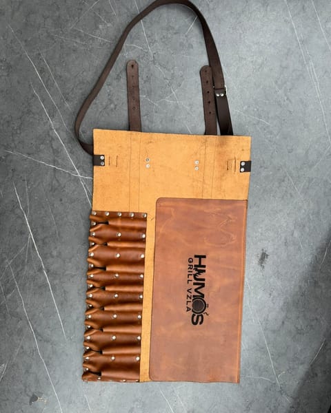 Estuche de cuchillos abierto, con los bolsillos y la tapa en cuero miel y un logo grabado