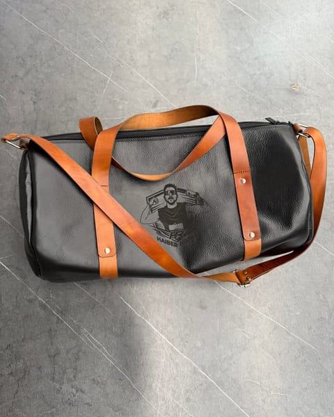 Maleta de cuero negro con correas miel y un retrato grabado