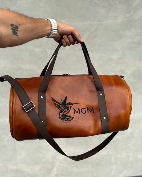 Maleta de cuero miel en la mano, con unas iniciales y un diseño grabados en el cuerpo