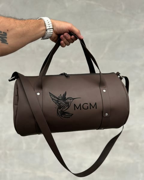Maleta de cuero café en la mano, con unas iniciales y un diseño grabados