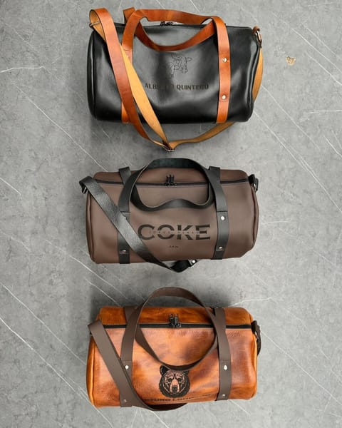 Tres maletas de cuero con nombres y diseños grabados: negro con correas miel, café con correas negras y miel con correas café