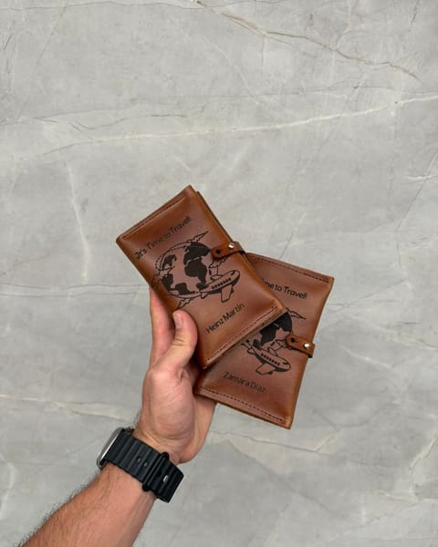 Dos portapasaportes dobles de cuero miel en la mano, con diseños de viaje grabados