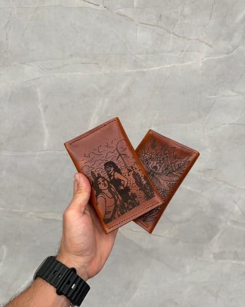 Dos portapasaportes dobles de cuero miel en la mano, por detrás, con un retrato y un diseño de flores grabados