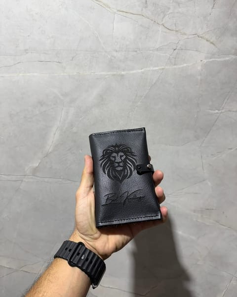 Portapasaporte doble de cuero negro en la mano, con un logo y un nombre grabados
