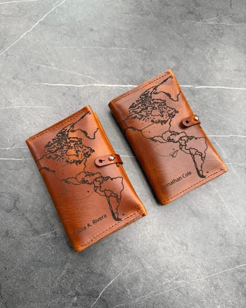 Dos portapasaportes dobles de cuero miel con el mapa del mundo y un nombre grabados