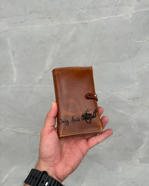Portapasaporte doble de cuero miel en la mano, con un nombre grabado